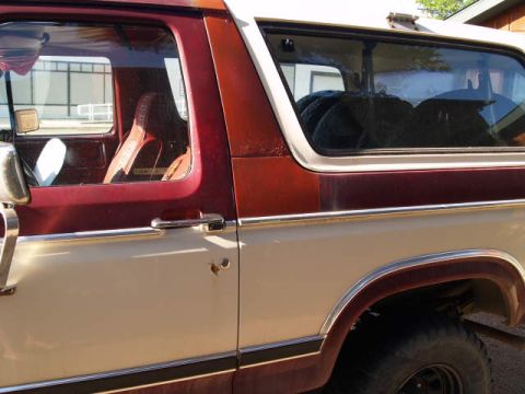 1996 Ford Bronco - Close-up side view of a two-tone red and tan Ford Bronco. The image shows the driver's side door, front fender, and rear wheel well.