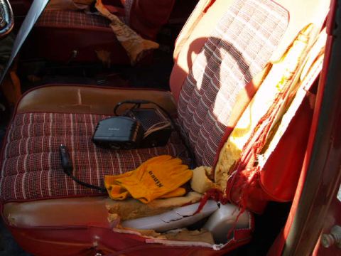 1996 Ford Bronco - The interior of a vehicle shows a worn red and brown plaid seat with a black electronic device plugged into a car charger. A pair of orange…