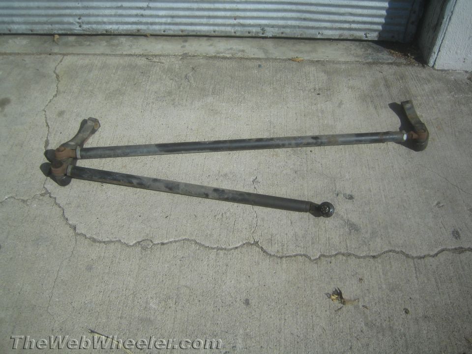 Two rusty steering linkage rods with tie rod ends lying on cracked concrete