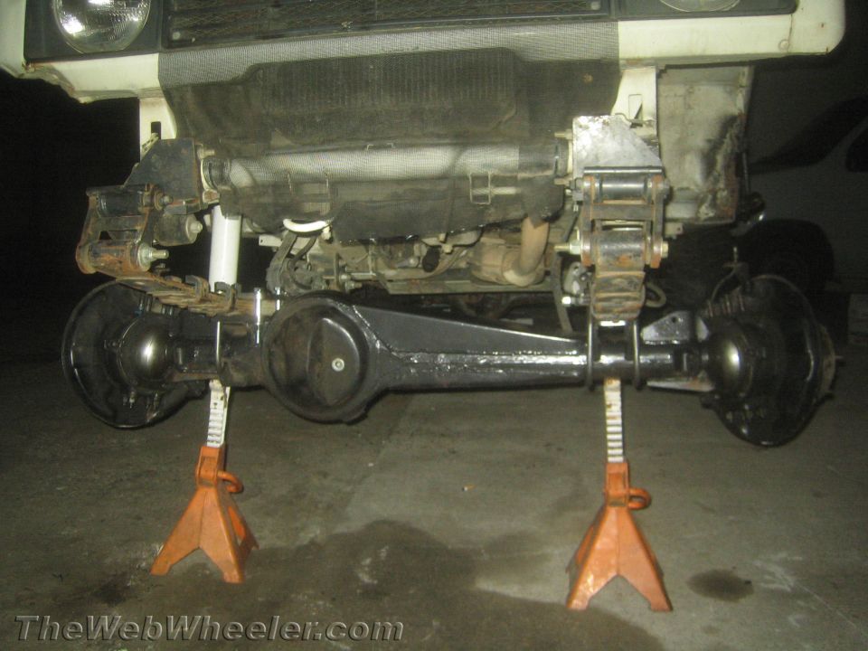 Front solid axle of a truck supported on orange jack stands in a shop