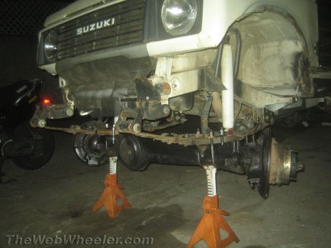 1987 Suzuki Samurai - Photo of a white Suzuki 4x4 supported on jack stands, exposing the front axle, drivetrain and suspension.