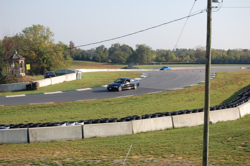 Black BMW coupe on a race track with a blue car in the distance.