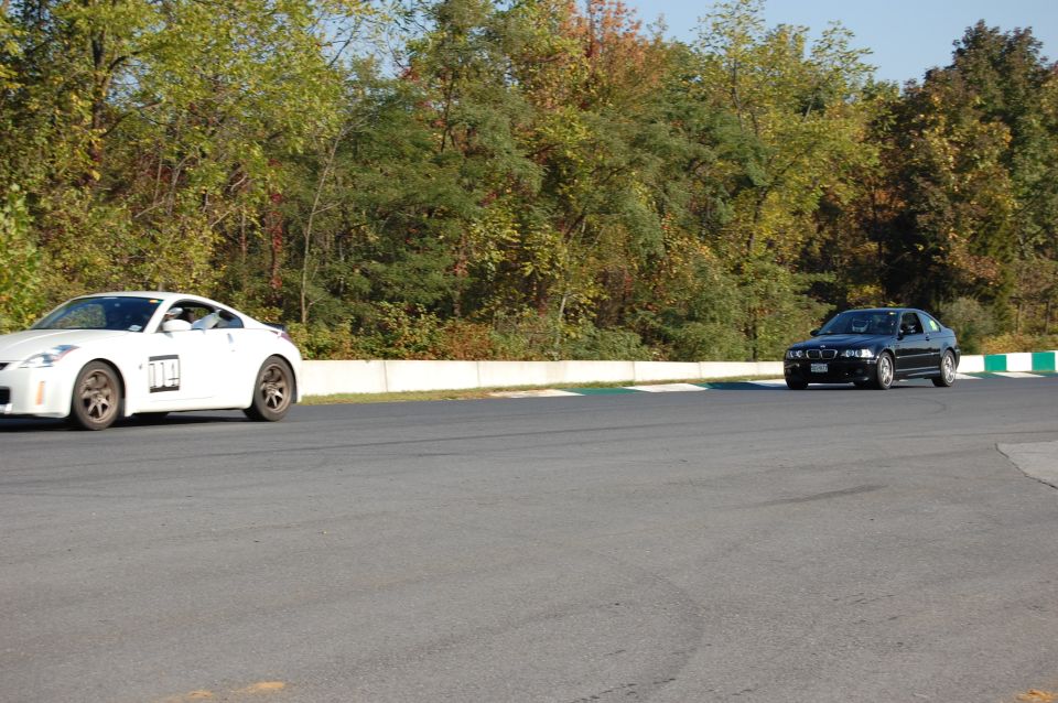 Black BMW M3 on a race track with a white Nissan 350Z in the background.