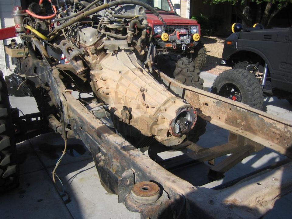Vehicle frame with engine and transmission assembly, with other off-road vehicles in background.