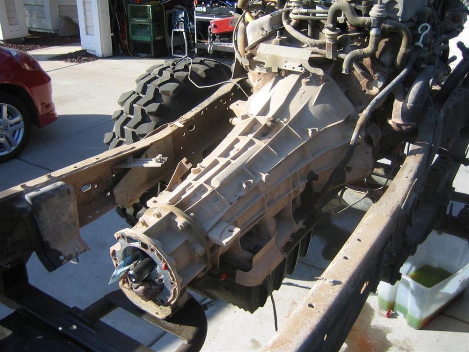 Dusty automatic transmission and transfer case in bare truck frame rails in a driveway