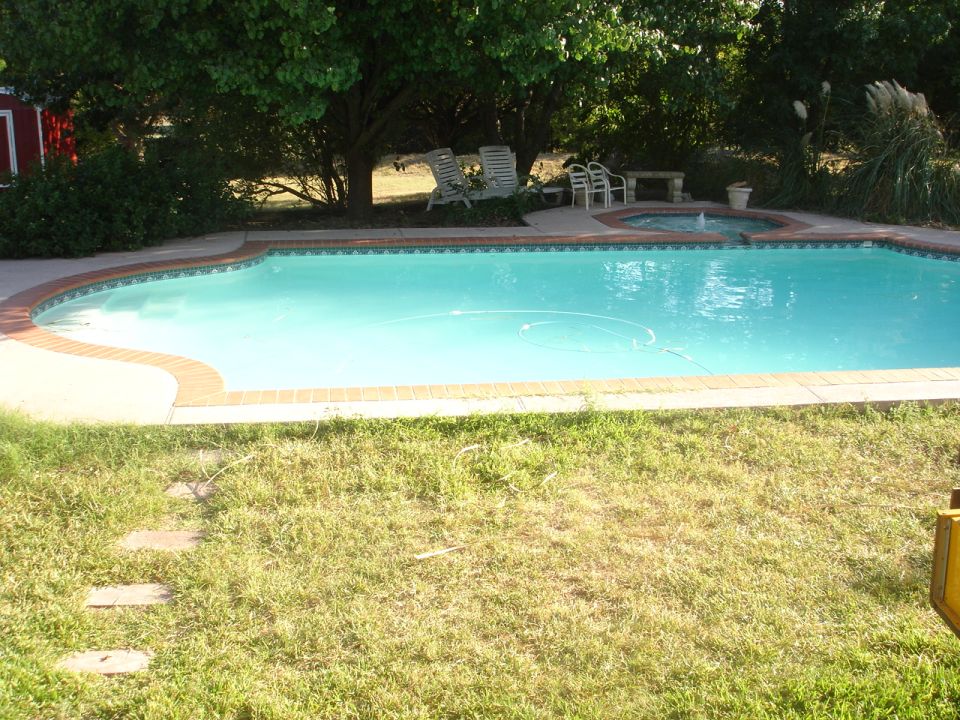 Swimming pool with hot tub and fountain in a grassy backyard.