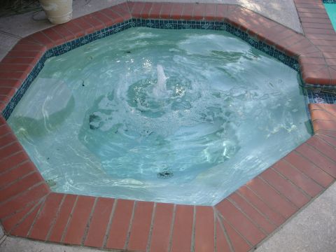 1989 Ford Bronco - A circular spa with a fountain in the center is surrounded by a brick border and blue tile accents.