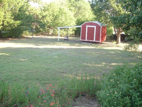 1989 Ford Bronco - A red storage shed with white trim sits in a grassy yard surrounded by trees. A white awning extends from the shed.