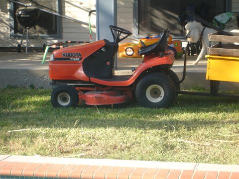 1989 Ford Bronco - An orange Kubota T1460 riding lawn mower is parked on a grassy area next to a concrete patio. A yellow utility trailer is attached to the r…