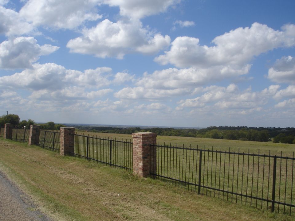 Black metal fence with brick posts in a grassy field under a cloudy sky.