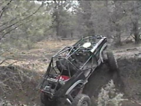 1984 Ford Bronco - A heavily modified off-road vehicle, likely a custom buggy built on a Bronco chassis, navigates a steep, muddy embankment. The vehicle feat…