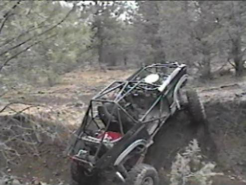 Custom off-road buggy with roll cage climbing a steep muddy bank.