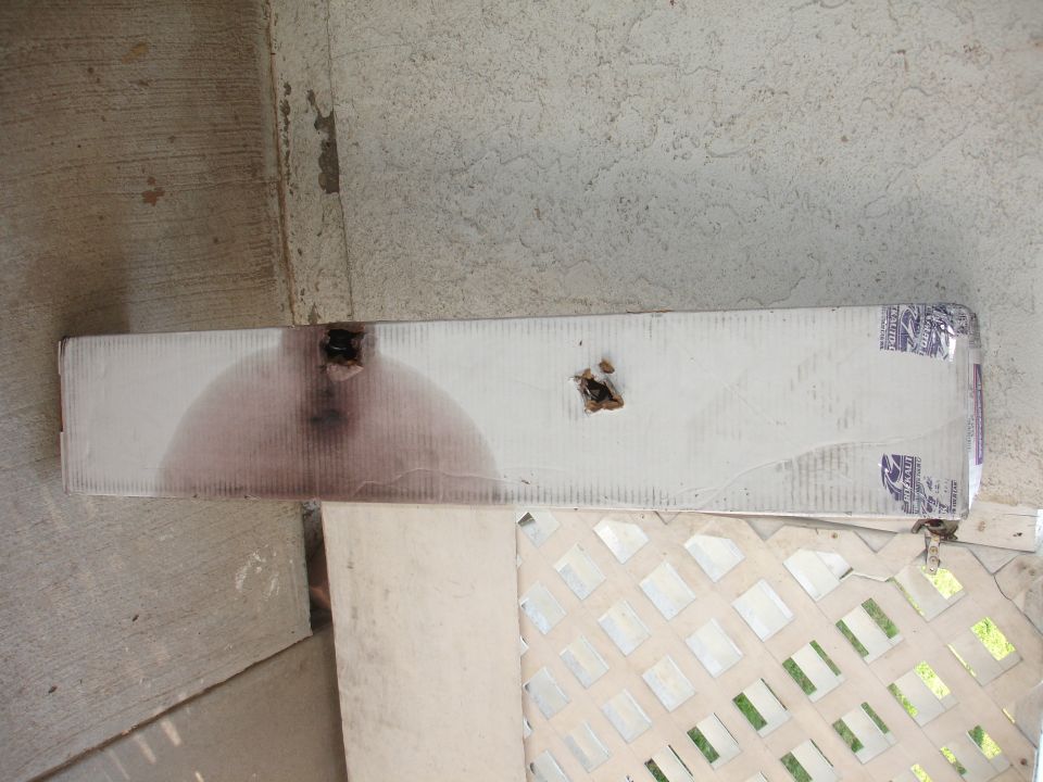 Damaged cardboard box with holes and stain on concrete.