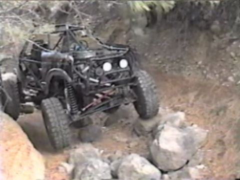 1984 Ford Bronco - A heavily modified off-road vehicle, identified as a 1984 Ford Bronco, navigates a rocky terrain with its tires angled to climb over large…