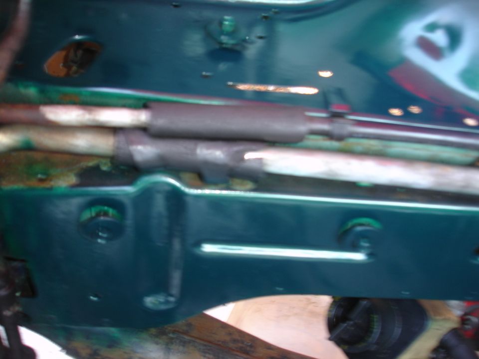 Underside of a vehicle showing green painted metal and two sleeved rods.