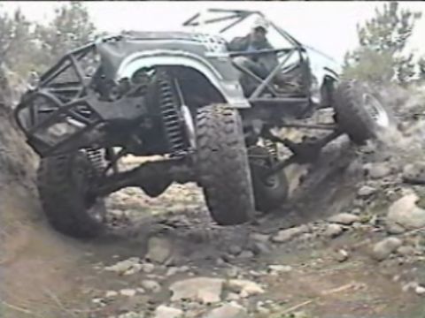 1984 Ford Bronco - A heavily modified off-road vehicle, likely a Ford Bronco, navigates a steep, rocky incline. The vehicle features a custom roll cage, large…