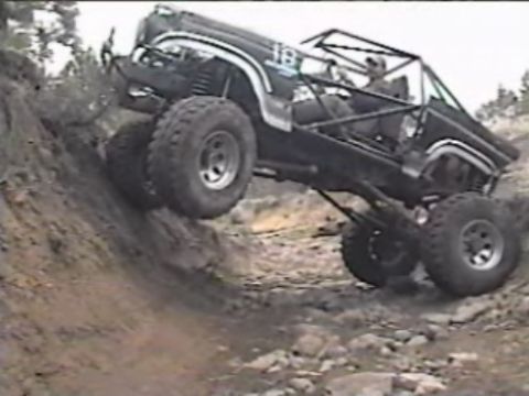 1984 Ford Bronco - A heavily modified black off-road vehicle, possibly a Ford Bronco, navigates a steep, rocky incline. The vehicle features a roll cage and l…