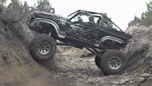 Modified black Ford Bronco climbing a steep rocky hill off-road.