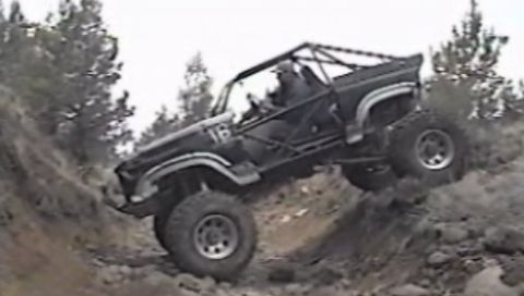 1984 Ford Bronco - A heavily modified black off-road vehicle, appearing to be a Ford Bronco, navigates a steep, rocky incline. The vehicle features a roll cag…