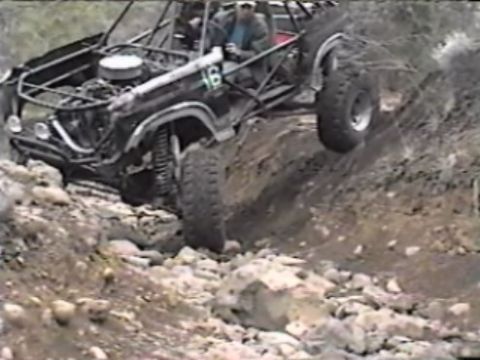 1984 Ford Bronco - A heavily modified off-road buggy, appearing to be based on a 1984 Ford Bronco, navigates a steep, rocky incline. The vehicle features a ro…