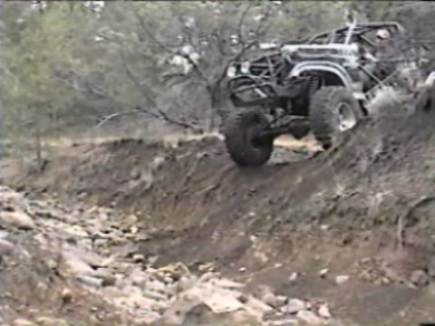 1984 Ford Bronco - A heavily modified 4x4 vehicle, likely a Ford Bronco, navigates a steep, rocky, and muddy incline in an outdoor, arid environment. The vehi…