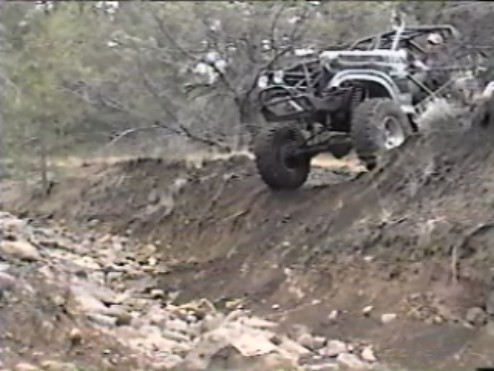 Modified 4x4 Bronco climbing a steep, muddy, and rocky hill.