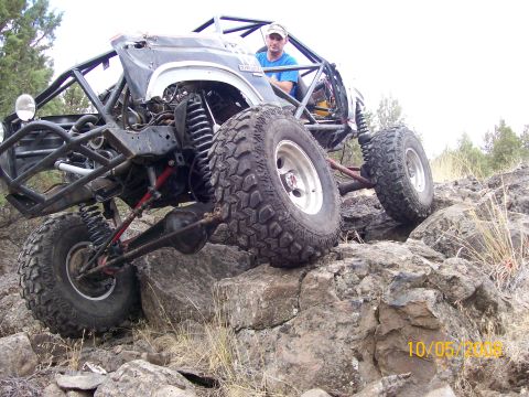 1984 Ford Bronco - A heavily modified off-road vehicle, likely a Ford Bronco, navigates a rocky terrain. The vehicle features a custom roll cage, large off-ro…