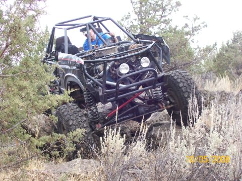 1984 Ford Bronco - A bodyless tube-frame rock buggy crawling over boulders in juniper and sagebrush country, articulating on coilover shocks with a driver in…