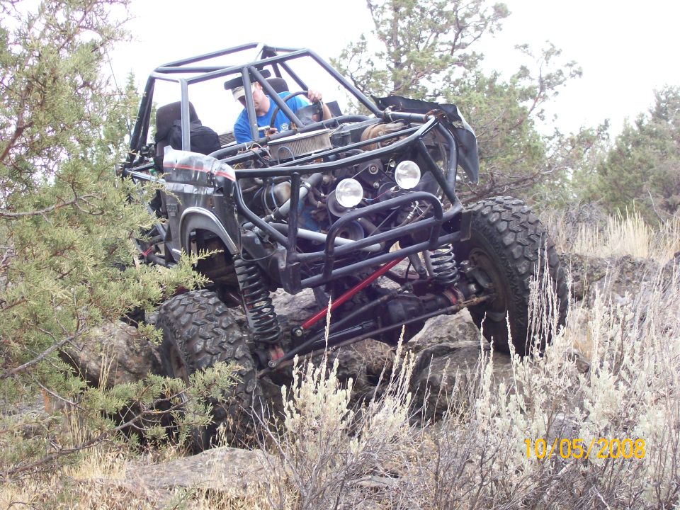 Tube-frame rock buggy with exposed V8 climbing boulders in sagebrush, driver at the wheel