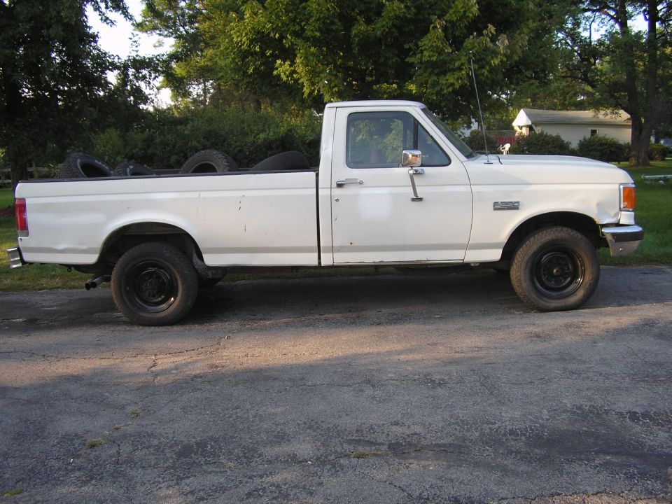Side view of a white 1990 Ford F-250 pickup truck with tires in the bed and black rims.