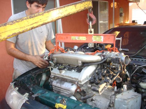 1993 Ford Taurus - A person uses an engine hoist to lift an engine out of a green vehicle during a rebuild.