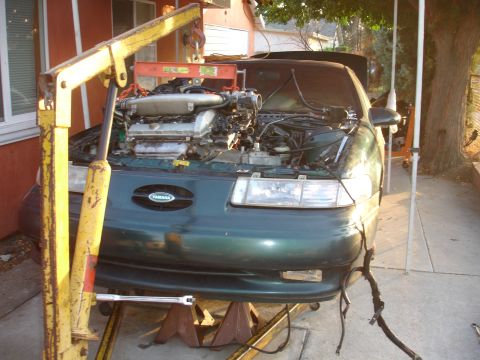 1993 Ford Taurus - A green sedan is parked on jack stands with its engine removed and an engine hoist attached to the engine bay.