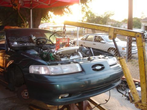 1993 Ford Taurus - A green sedan is undergoing engine work, supported by a yellow engine hoist and jack stands.
