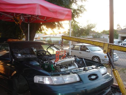 1993 Ford Taurus - A 1993 Ford Taurus is undergoing engine work, with its hood open and engine exposed, while another car is parked in the background.
