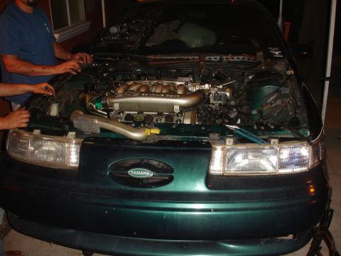 1993 Ford Taurus - Two people are working on the engine of a green sedan with its hood open.