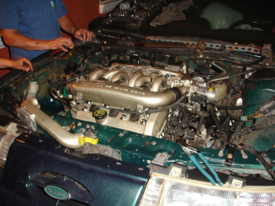 Green 1993 Ford Taurus engine bay with V6 engine, tools, and two people working