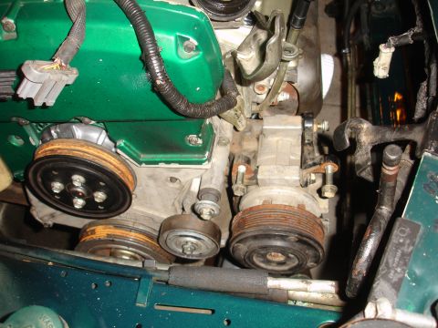 1993 Ford Taurus - Close-up view of an engine compartment, highlighting the green valve cover, various pulleys, and the air conditioning compressor.