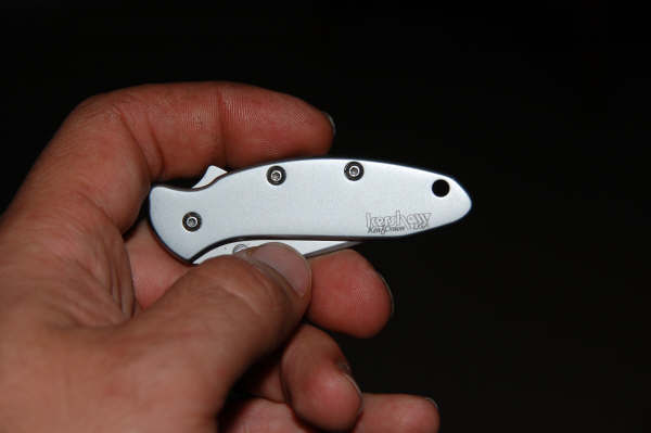 Silver Kershaw pocket knife with black handle, held in a hand against a dark background