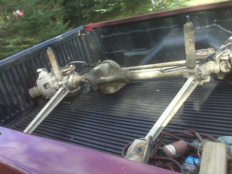 Rear axle assembly with shocks, sitting in the bed of a pickup truck