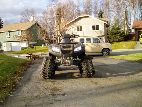 2000 Ford E350 - All-terrain vehicle equipped with tracks instead of wheels is parked in a residential driveway.
