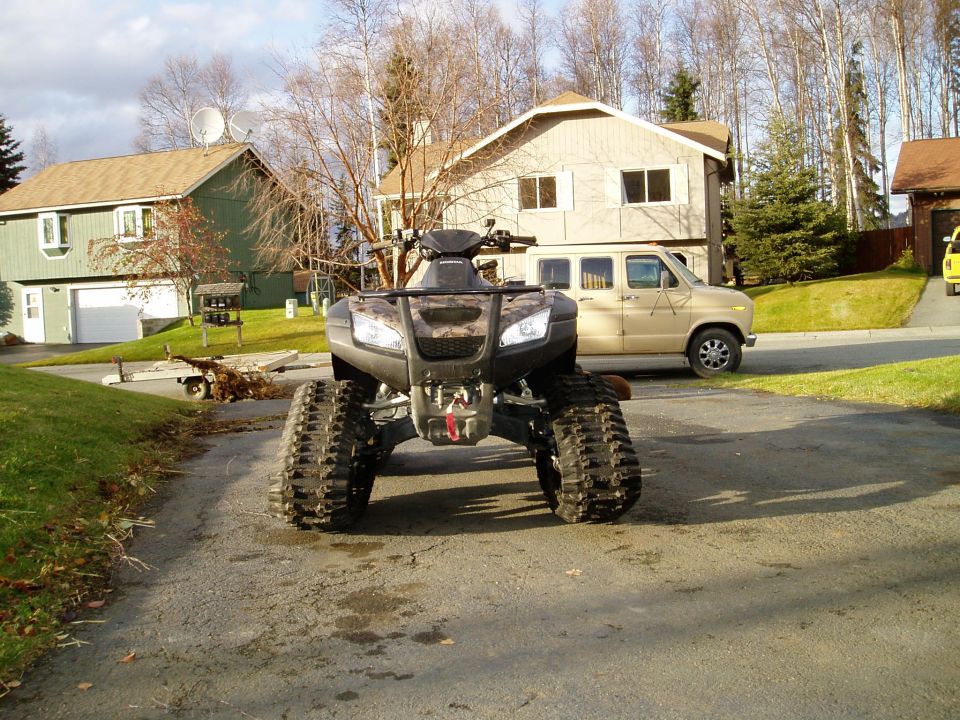 Front view of ATV with tracks, parked in driveway with a van in background