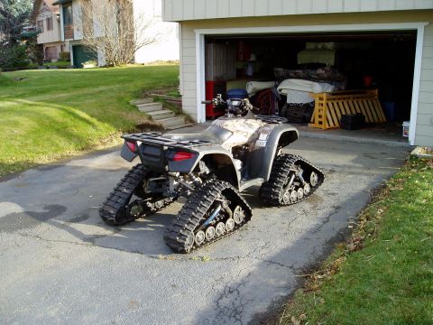2000 Ford E350 - An all-terrain vehicle is equipped with tracks for snow or rough terrain, parked outside a garage.