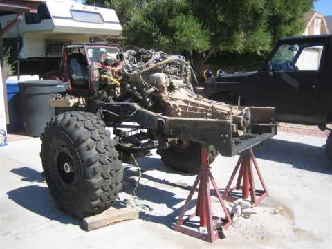 1994 Ford Bronco - The chassis of a vehicle is elevated on red jack stands, with its engine and drivetrain components exposed. Another vehicle is visible in t…