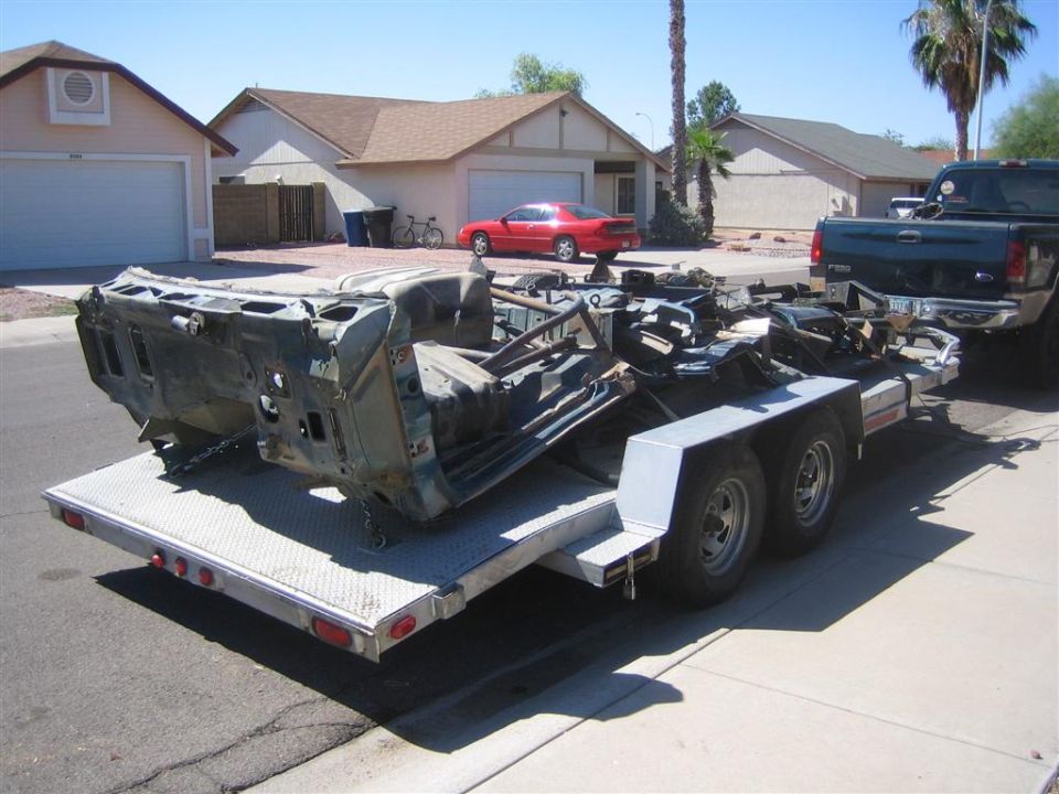 Car chassis and frame loaded onto a dual-axle trailer, being towed by a pickup truck