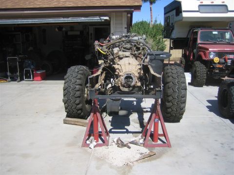 1994 Ford Bronco - Vehicle chassis undergoing repair with engine exposed and large off-road tires, other vehicles parked nearby.