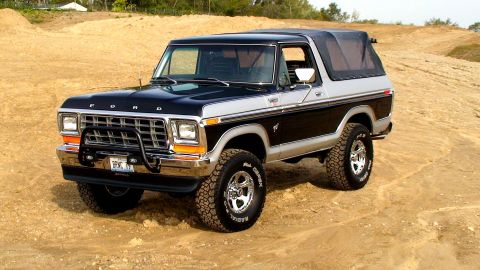 1979 Ford Bronco - This two-tone Ford Bronco is parked on a dirt lot with a wooded area in the background.
