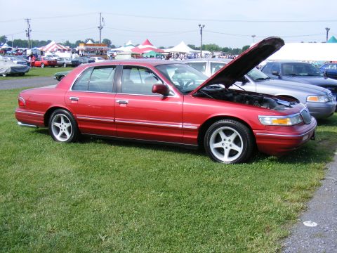 1997 Mercury Grand Marquis - A red sedan with its hood open is parked on grass at an outdoor event.