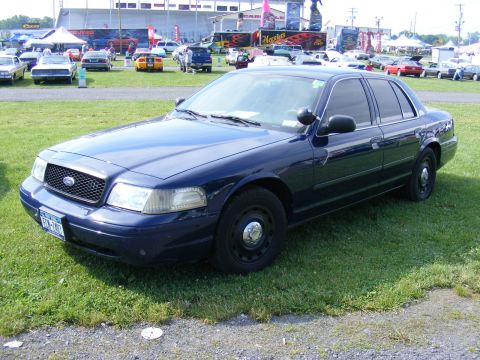 1997 Mercury Grand Marquis - A dark blue Ford Crown Victoria is parked on a grassy area with tents and other vehicles in the background.