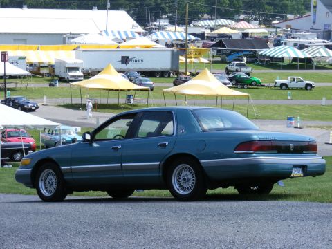 1997 Mercury Grand Marquis - A teal sedan is parked at an outdoor event with tents and other vehicles visible in the background.