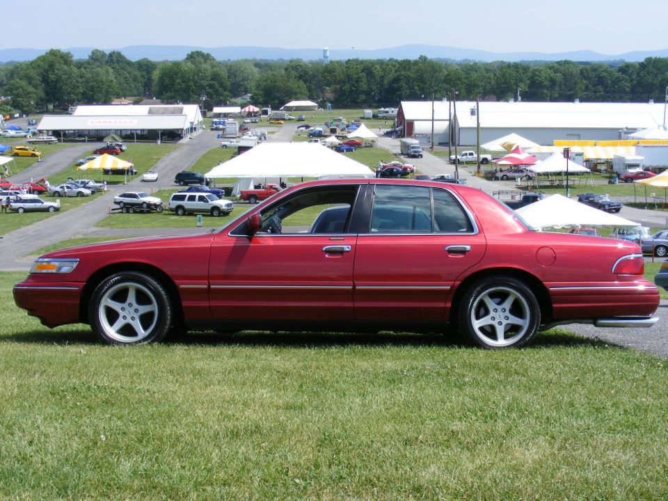 Red 1997 Mercury Grand Marquis sedan, side view, at an outdoor event